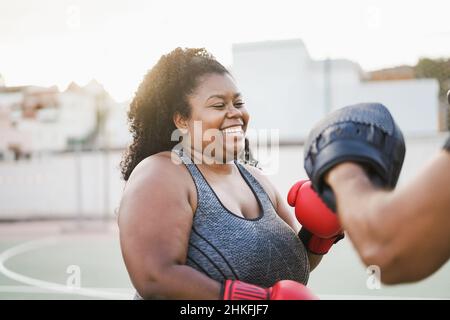 African curvy woman and personal trainer doing boxing workout session outdoor - Focus on face Stock Photo
