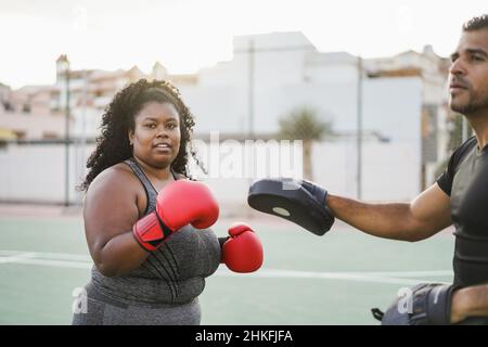 African curvy woman and personal trainer doing boxing workout session outdoor - Focus on girl face Stock Photo