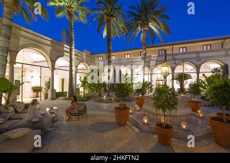 Italy, Sicily, Taormina, San Domenico Palace hotel, women having an aperitif in the cloister flanked by palm trees and illuminated at nightfall in this former Dominican convent transformed into a legendary hotel owned by the Four Seasons group Stock Photo