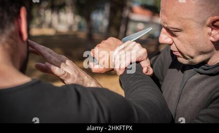 Knife threat. Kapap instructor demonstrates martial arts self defense disarming technique against knife attack. Weapon disarm training. Demonstration Stock Photo