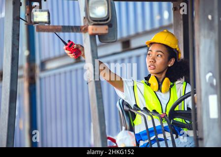 Female foreman use radio communication to communicate while driving forklift at shipping container yard. shipping in docks. Stock Photo