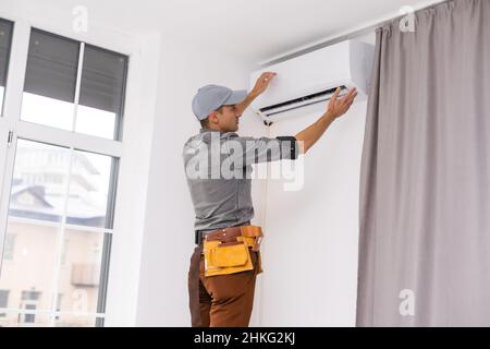 Young Man Repairing Air Conditioner Standing On Stepladder Stock Photo