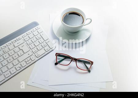 Computer keyboard, coffee cup and red glasses on white blank paper and a light gray desk, office work concept, copy space, selected focus, narrow dept Stock Photo