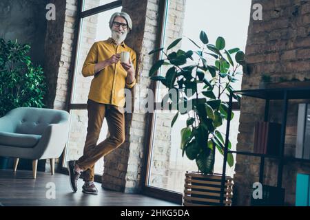 Photo of positive senior man wear yellow shirt glasses drinking tasty coffee having rest indoors workshop workstation Stock Photo
