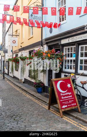 Many colourful hanging baskets of flowers hang outside The Mad Merchant cafe and Tudor Rose tearoom in The Barbican in Plymouth. Stock Photo