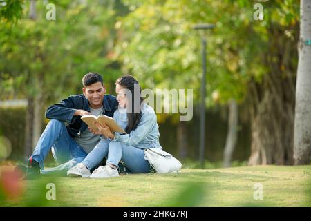 Friends spending time on college campus and reading book together Stock Photo