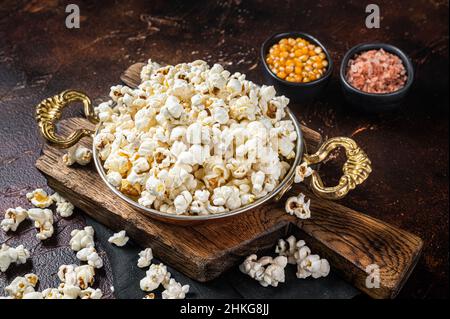 Prepared salty popcorn in a skillet and corn kernel. Dark background. Top view Stock Photo