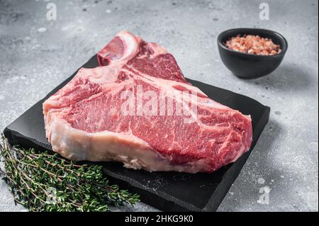 Raw dry aged wagyu porterhouse beef steak, uncooked T-bone on marble board with thyme. Gray background. Top view Stock Photo
