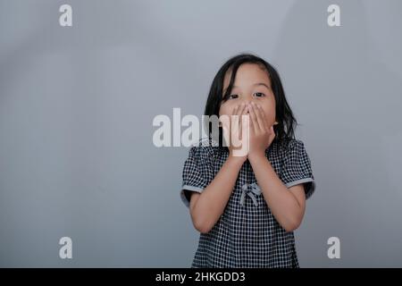 Surprised by a beautiful little girl with long hair looking at the camera in grey background. Little girl's emotions and facial expressions Stock Photo