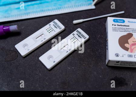 A positive result rapid Covid test, also known as antigen test or lateral flow test, is seen in a close up on a black table with a face mask and syrin Stock Photo