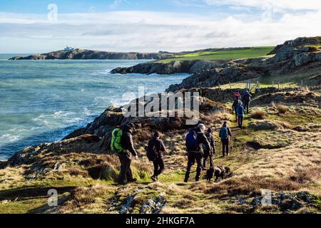 Walkers walking from Amlwch to Llaneilian along Anglesey Coastal Path with view along rocky coast to Point Lynas. Isle of Anglesey, north Wales UK Stock Photo