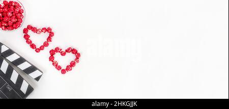Valentine's Day movie concept. Clapperboard with hearts made of red caramel popcorn with copy space on a white background. Stock Photo