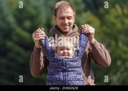 Father lifting a cheerful toddler daughter outdoors in nature Stock Photo