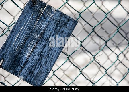 Close-up of an old cracked rectangular wooden slab on a green mesh fence Stock Photo