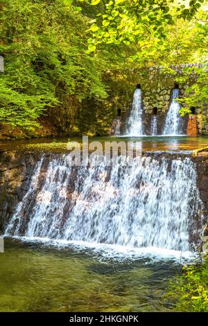 Artificial weir on a river in a leafy forest. Stock Photo