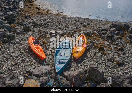 Three colourful kayaks tethered on a rocky beach at Porth Dinllaen, Wales Stock Photo