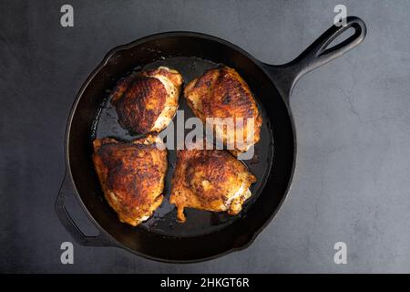 Overhead View of Spice-Rubbed Chicken Thighs in a Cast Iron Skillet: Roasted bone-in skin-on chicken thighs roasted in a cast-iron frying pan Stock Photo