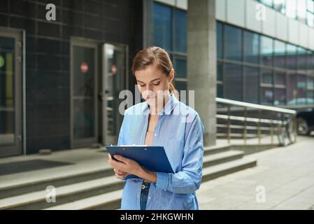 Professional young lawyer woman standing in front of court and holding legal documents waiting for customers ready to handle case. Outdoor. Stock Photo