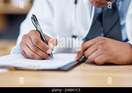 Updating his notes. Closeup shot of an unrecognisable doctor writing notes on a clipboard in an office. Stock Photo