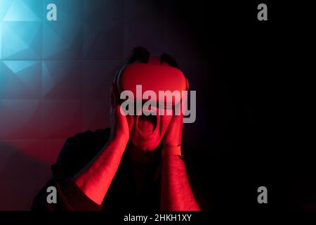 Man in white virtual reality goggles screaming in fear in red light Stock Photo