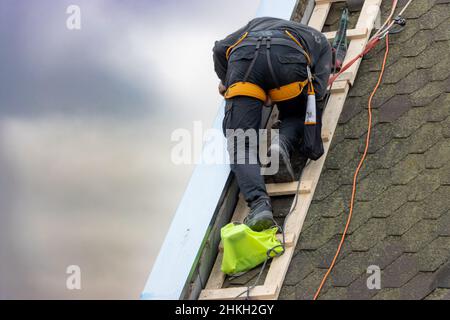 A man works on the roof repair, installs sheet metal on top of the gable wall Stock Photo