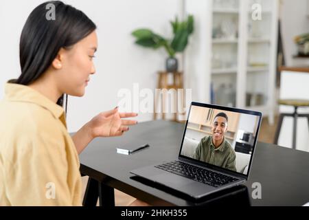 Video call. Asian woman wearing smart casual wear using laptop for talking with a male colleague, an online teacher or mate via video Stock Photo