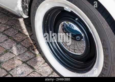 Close-up view of a vintage car tire with a chrome-plated hubcap and the mirror image of another German vintage car that can be seen in it. Stock Photo