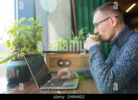 Portrait of modern bearded businessman working with laptop and drinking coffee. Stock Photo