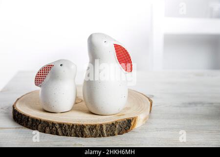 Two figurines of white hares with red ears big and small on a wooden saw cut and a bowl with eggs in the background in a white Scandinavian style kitc Stock Photo