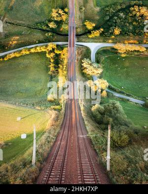 Railway with bridge and road among green fields in warped perspective, Poland Stock Photo