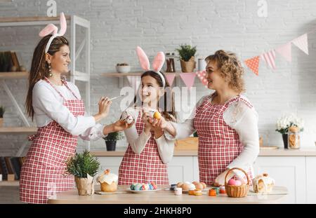 Mother and daughters draw Easter eggs. A happy family is preparing for Easter. Stock Photo