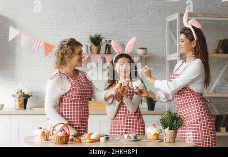 Mother and daughters draw Easter eggs. A happy family is preparing for Easter. Stock Photo