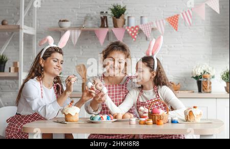 Mother and daughters draw Easter eggs. A happy family is preparing for Easter. Stock Photo
