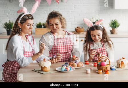 Mother and daughters draw Easter eggs. A happy family is preparing for Easter. Stock Photo