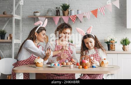Mother and daughters draw Easter eggs. A happy family is preparing for Easter. Stock Photo