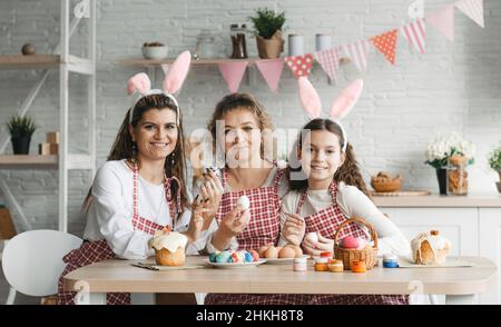 Mother and daughters draw Easter eggs. A happy family is preparing for Easter. Stock Photo