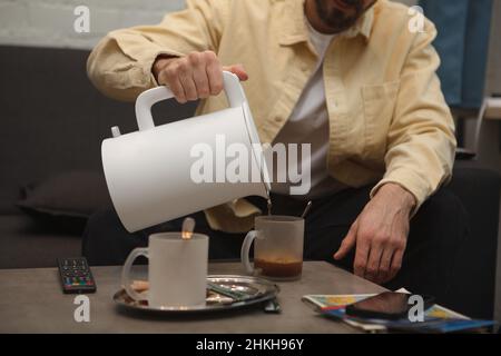 Cropped shot of a man pouring hot water from electric kettle into his cup Stock Photo