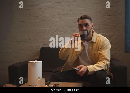 Handsome man watching tv while drinking coffee on a couch Stock Photo