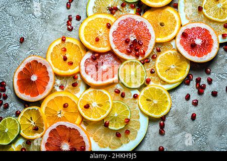 diagonal composition of slised citruses, lemon, lime, orange and pomegranate seeds on a rustic beige cement background, top view. Stock Photo