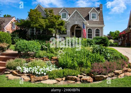 Grey multiple gable brick house with colorful rock garden in front flying American flag Stock Photo