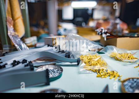 A lot of different metal bolts and nuts, plastic small components and professional tools lie on a blue desktop in a master worker's workshop under a c Stock Photo