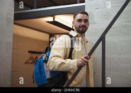 Handsome bearded male tourist with a backpack walking up the stairs at his hotel room Stock Photo