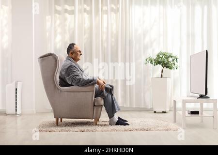 Profile shot of a mature man in a bathrobe sitting in an armchair and watching tv at home Stock Photo