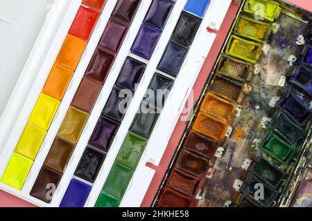 New and old set of watercolor palette top view. Used watercolor cuvettes and new ones. Watercolor paints close up. Materials for painting with paints. Stock Photo