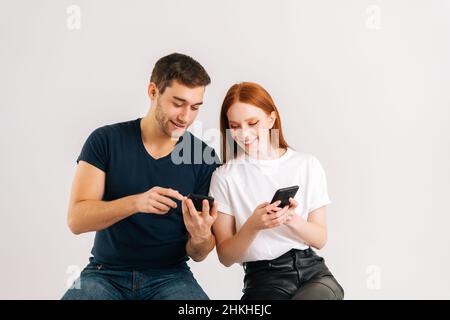 Studio shot of young handsome man showing new mobile software app to smiling girlfriend on white isolated background. Stock Photo
