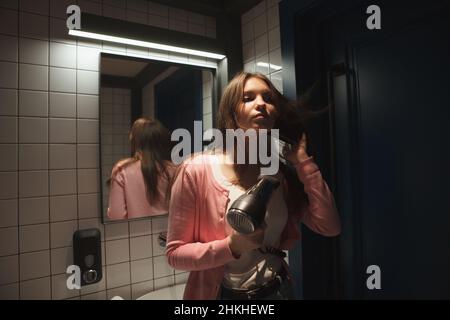 Woman blow drying her hair in the bathroom Stock Photo
