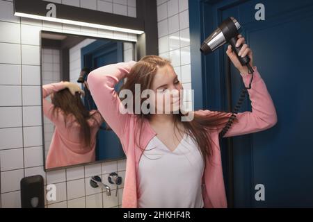 Charming young woman blow drying her hair in the bathroom Stock Photo
