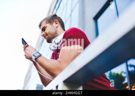 Positive young guy messaging via smartphone while leaning on railing Stock Photo