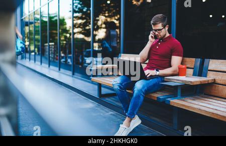 Serious male freelancer using laptop while talking on phone Stock Photo