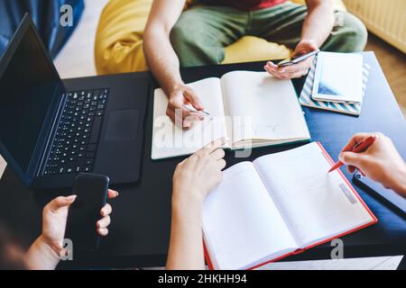 Crop students doing homework together in workplace Stock Photo